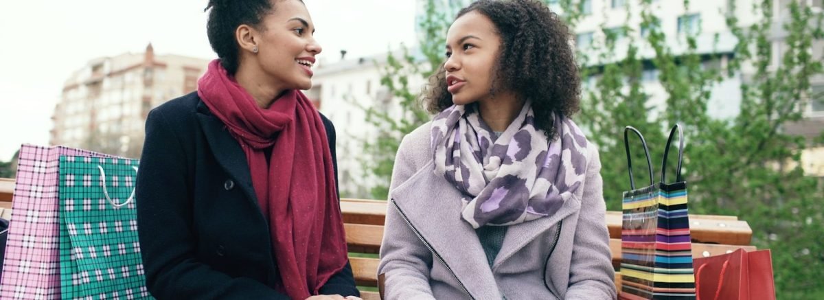Two women sitting on a bench with shopping bags.